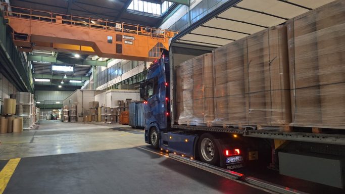 Lkw entlädt Holzpaletten in einer Lagerhalle mit Kranausrüstung.