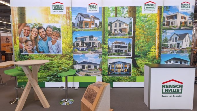 Messestand mit Bildern von modernen Häusern und einer Familie in einem Garten.