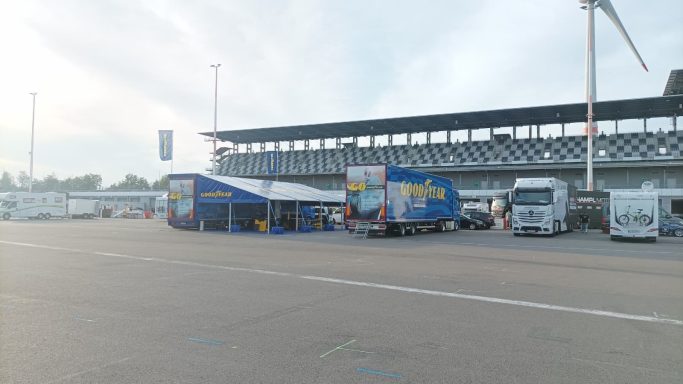 Zelt und Lkw auf einem Parkplatz vor einer Tribüne, Wolken am Himmel.
