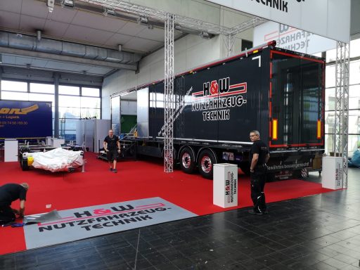 Lkw mit schwarzem Auflieger, rotem Teppich und Ausstellungsstücken in einer Halle.