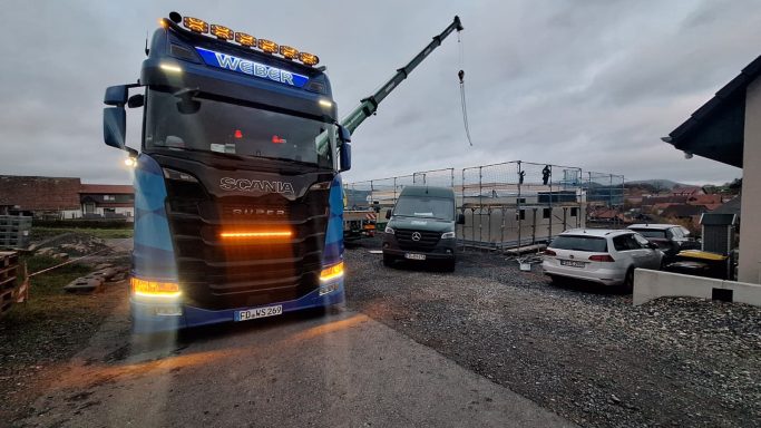 Ein großer Lkw steht auf einer Baustelle, im Hintergrund ein Kran und mehrere Fahrzeuge.