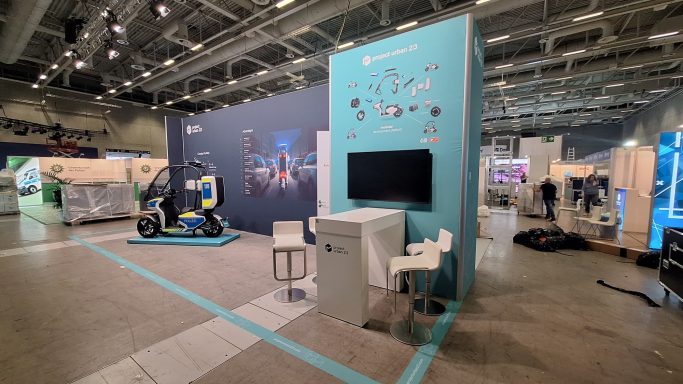 Messestand mit Regalen, Monitor und Ausstellungsfläche in einem großen Veranstaltungsraum.