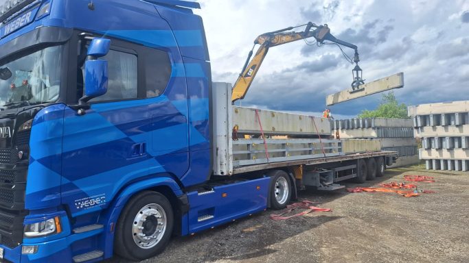 Blauer Lastwagen mit Kranausleger, der Baumaterialien entlädt.
