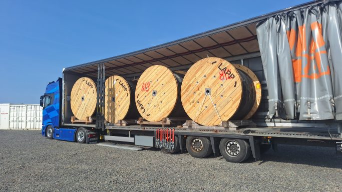 Lkw mit Holzrollen auf einem Anhänger, geparkt im Freien.
